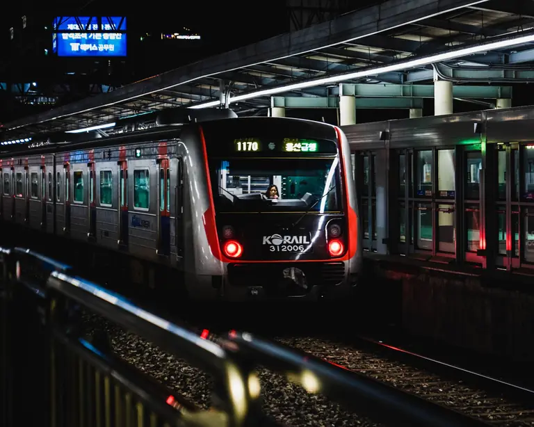 A Korail train at night in a bustling Seoul station, illuminated with vibrant lights.