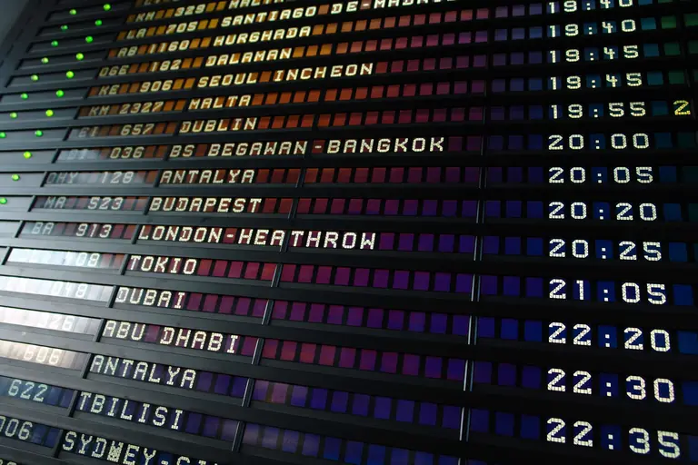 Retro flip-style airport departure board showing international flight destinations and times.