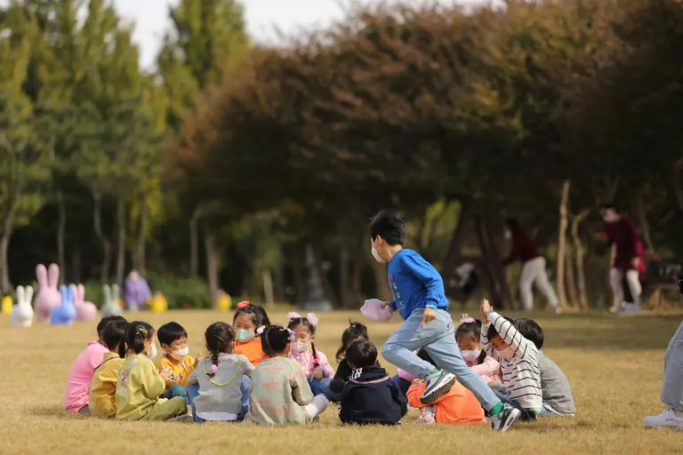 Group of children having fun outdoors in a park wearing face masks.