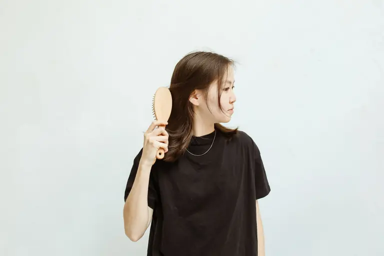 A young woman in a black shirt combs her hair against a white background.