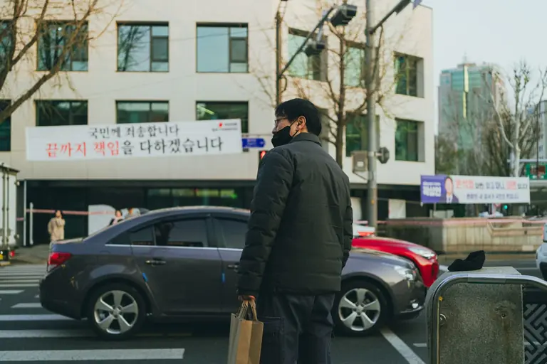 A pedestrian wearing a mask crosses a busy street in Seoul, capturing urban life.