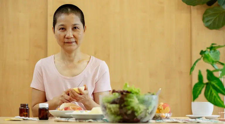 Cheerful ethnic ill female with short hair suffering from cancer at table with jars of medicines in daytime