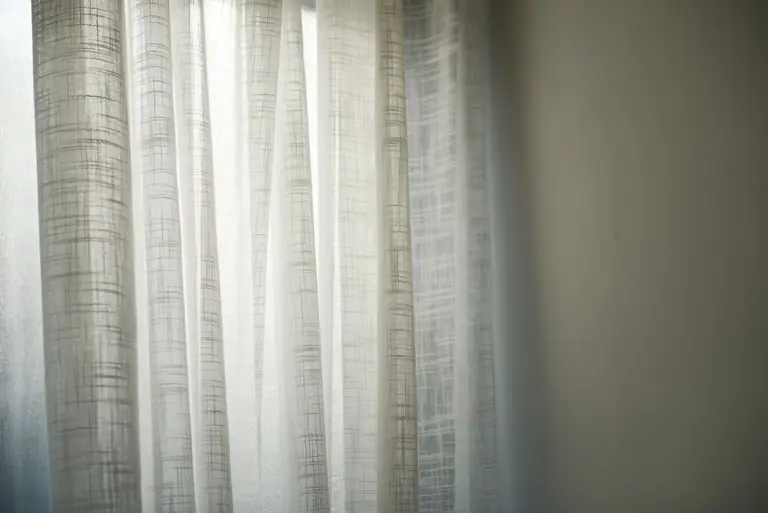 Sheer white curtains gently lit by daylight create subtle shadows on the wall.