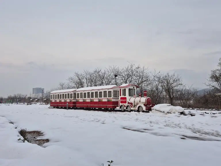 A red and white tourist train sits in a snowy park landscape in Gyeonggi, South Korea.