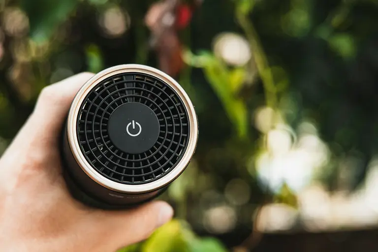 Crop anonymous person demonstrating modern wireless portable speaker with power button against blurred plants