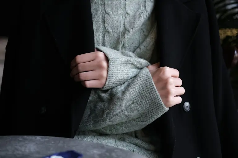 Close-up of hands wearing a knitted sweater under a black coat, showcasing winter fashion.