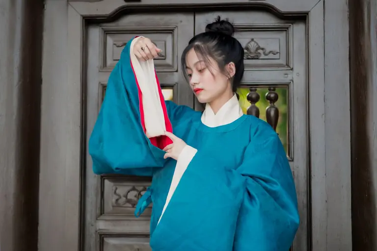 Asian woman in traditional Vietnamese attire standing by ornate wooden doors.