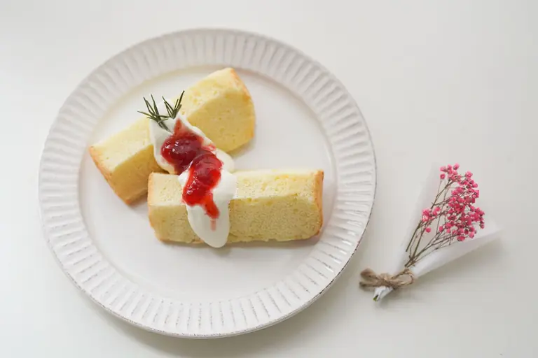 Two slices of sponge cake topped with cream and jam on a stylish plate.