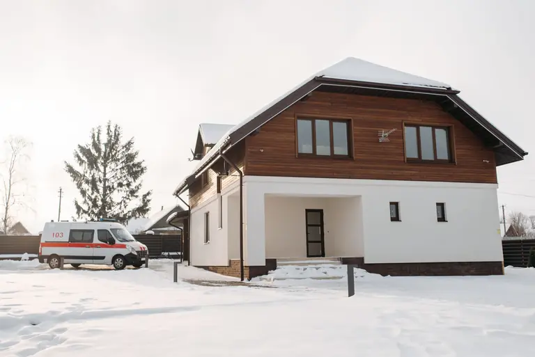 A suburban house with a snowy landscape and an ambulance parked nearby.
