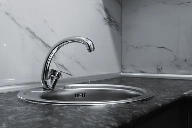 A stylish stainless steel kitchen faucet with a sleek and modern design set against a marble backsplash.