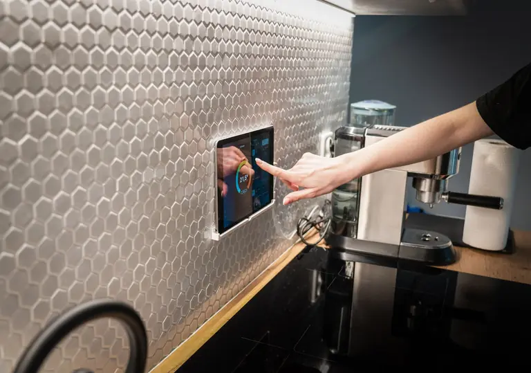 A modern kitchen with a touchscreen smart home control panel integrated into a hexagon-patterned wall.