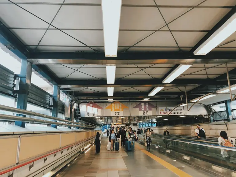 People navigate a busy walkway at Shibuya Station, Tokyo, with signage overhead.