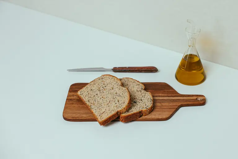 Sliced whole wheat bread on a wooden board with olive oil and knife.
