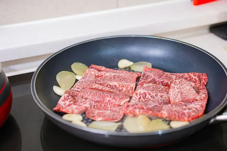 Meat and garlic are being cooked in a pan.