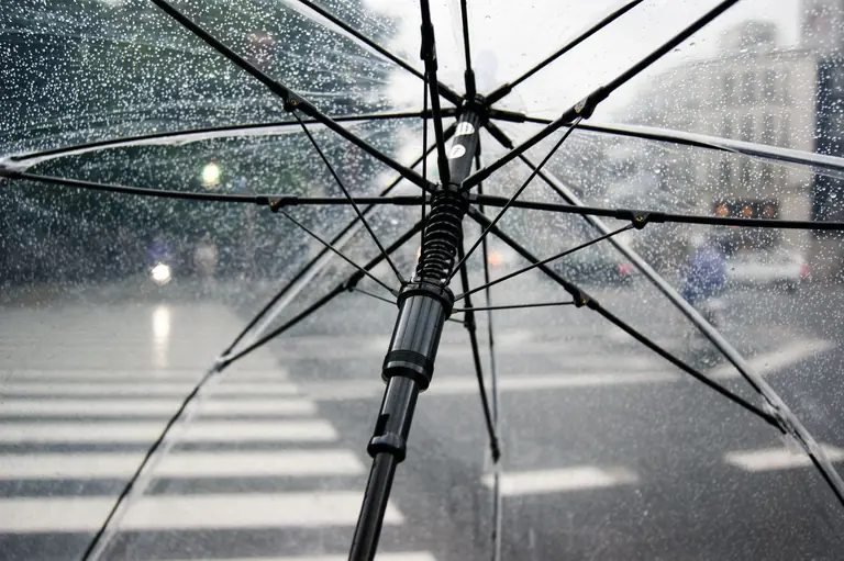 Close-up of a transparent umbrella with raindrops in an urban street setting.