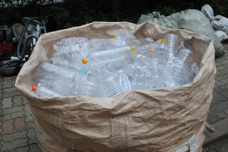 A filled bag of plastic bottles ready for recycling in an outdoor setting.