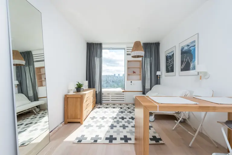 Wooden table and drawer placed in room with big window and wall decorated with pictures in light room with mirror