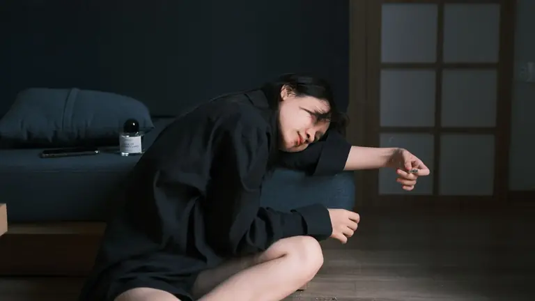Young woman in relaxed pose on floor beside sofa in dimly lit room.