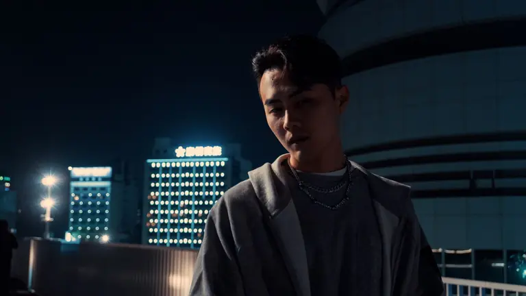 A man's thoughtful gaze during a city night scene, conveying introspection.