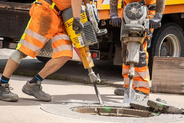Construction workers repairing road with heavy tools, emphasizing urban development.