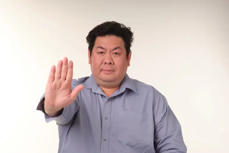 Portrait of a man in blue shirt gesturing stop with hand, studio background.