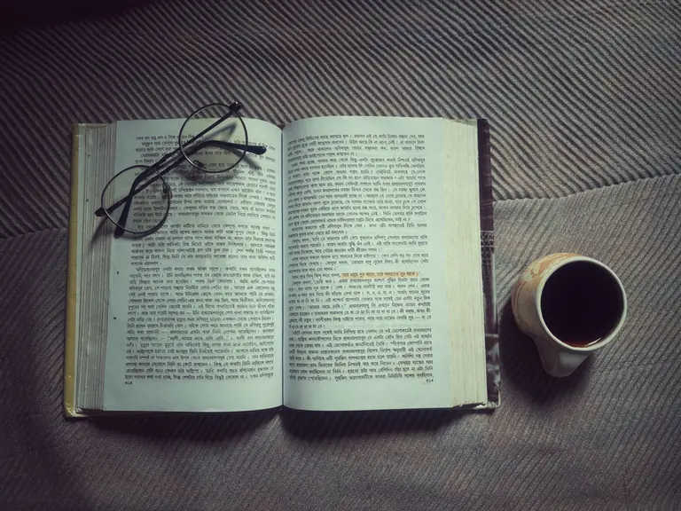 Open Hindi book with glasses and coffee cup on blanket, inviting cozy reading moment.