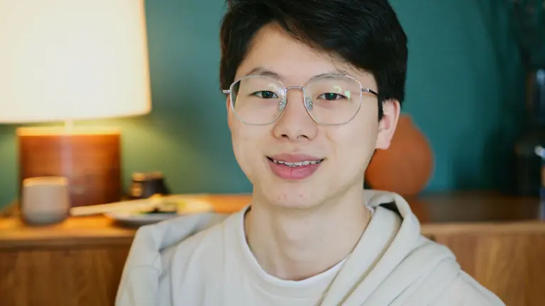 Close-up portrait of a smiling young Asian man wearing glasses, indoors.