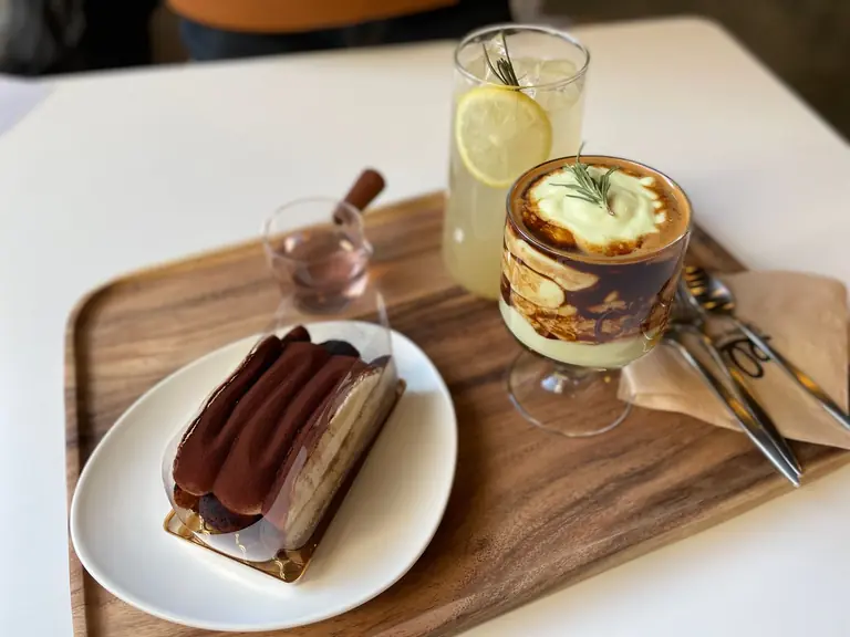 Close-up of a tiramisu and coffee on a wooden tray with lemon drink, creating a cozy food arrangement.