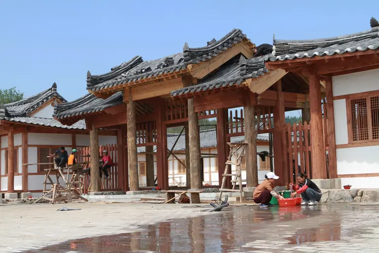Workers engaged in building a traditional Asian temple with wooden architecture, captured outdoors.