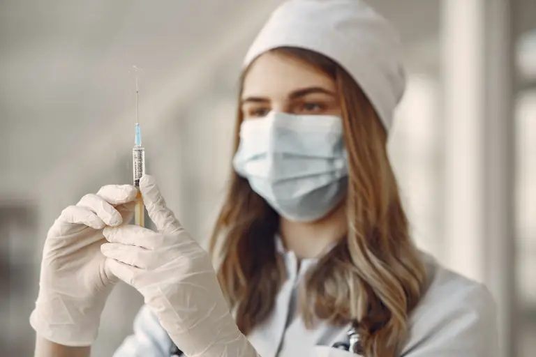 A female doctor in a face mask fills a syringe with vaccine indoors, emphasizing healthcare and safety.