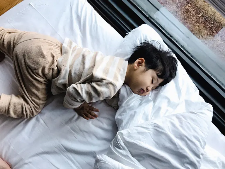 An Asian child peacefully sleeping in cozy pajamas by a window, indoors.