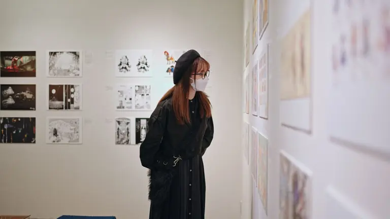 A woman in a mask examines art in a Shinjuku gallery, Tokyo, Japan.