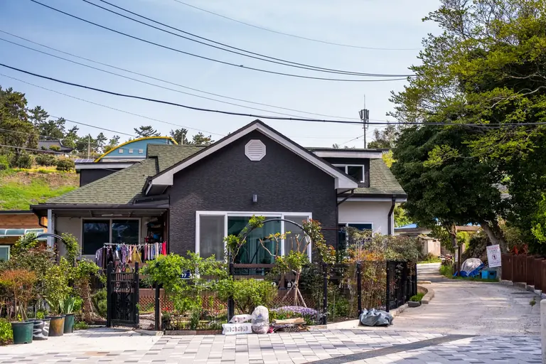 A charming suburban house with a lush front garden and laundry hanging outside on a sunny day.