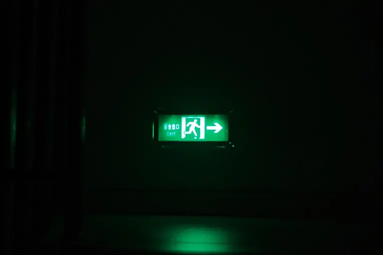 Illuminated green exit sign with directional arrow in a dark indoor setting.