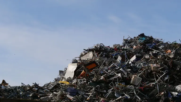 A vast pile of metal scrap and debris under a clear sky, captured at a junkyard.