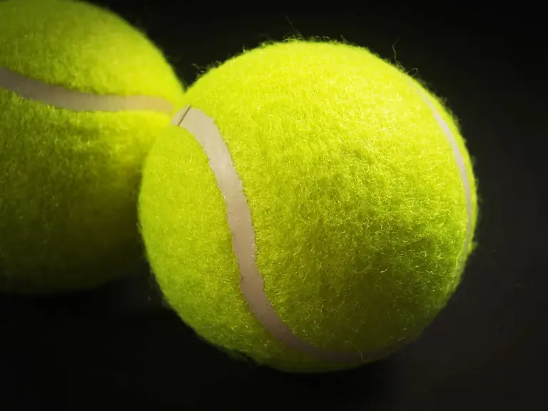 Close-up of two bright yellow tennis balls against a dark backdrop, showcasing texture and detail.