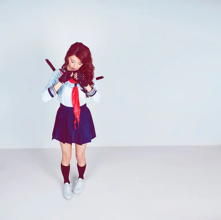 A young woman in a schoolgirl cosplay stands with swords in a studio setting.