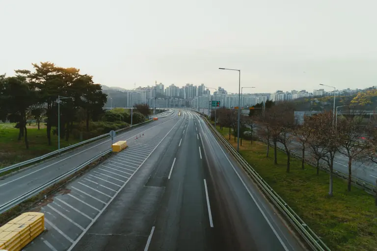 Peaceful view of an empty highway leading to Seoul city skyline with surrounding trees.