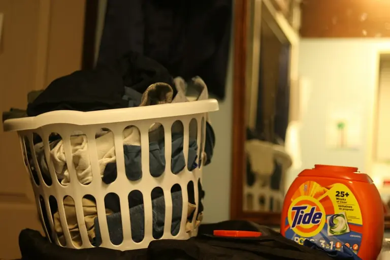 a laundry basket filled with clothes next to a bottle of tide