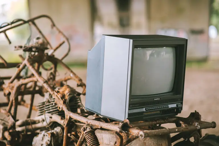 Small black old fashioned derelict television placed under concrete bridge on metal structure with corrosion on street against blurred background