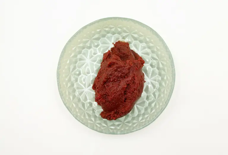 Red paste displayed in a textured glass bowl on a white background, captured overhead.