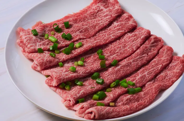 Slices of marbled Wagyu beef arranged on a plate with green onion garnish, ideal for gourmet cooking.