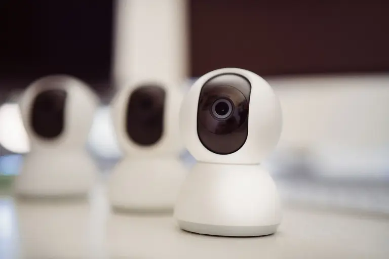 Close-up of three smart home security cameras placed on a white desk indoors.