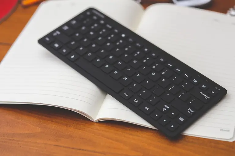 A wireless keyboard resting on an open notepad, perfect for modern desk setups.