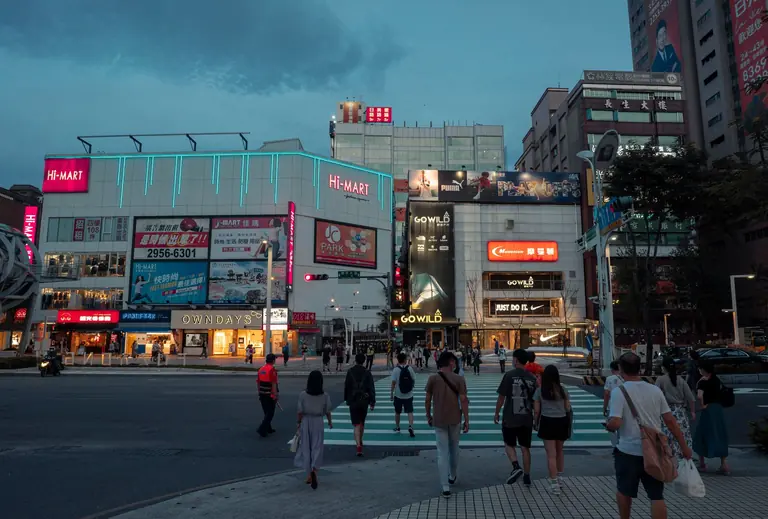 City street scene at dusk featuring a bustling pedestrian crossing and illuminated shops.
