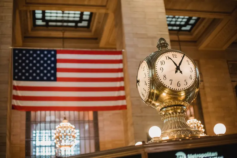 From below of golden old fashioned clock placed in building with ornamental walls against American flag placed in Grand Central Terminal in New York City