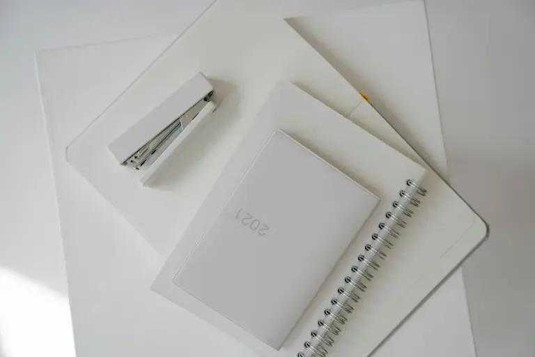 Top view of notebook and diary with white stapler located on opened planner with blank pages against white background