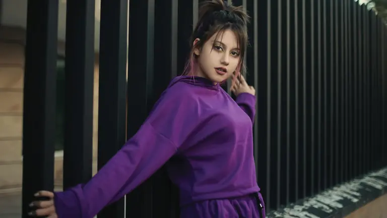 a woman leaning against a fence wearing a purple outfit