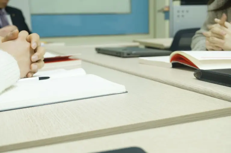 Close-up of a professional meeting setup with hands, laptops, and notebooks on a wooden desk.