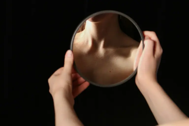 Hands hold a mirror reflecting a person's neck.
